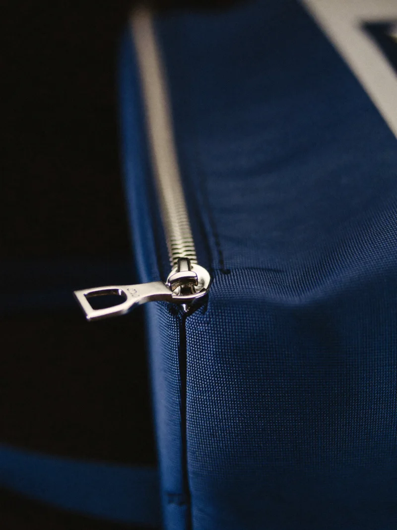 Makroaufnahme von Nylongewebe, Metallzipper und Naht eines Reiseetuis in Kobaltblau.