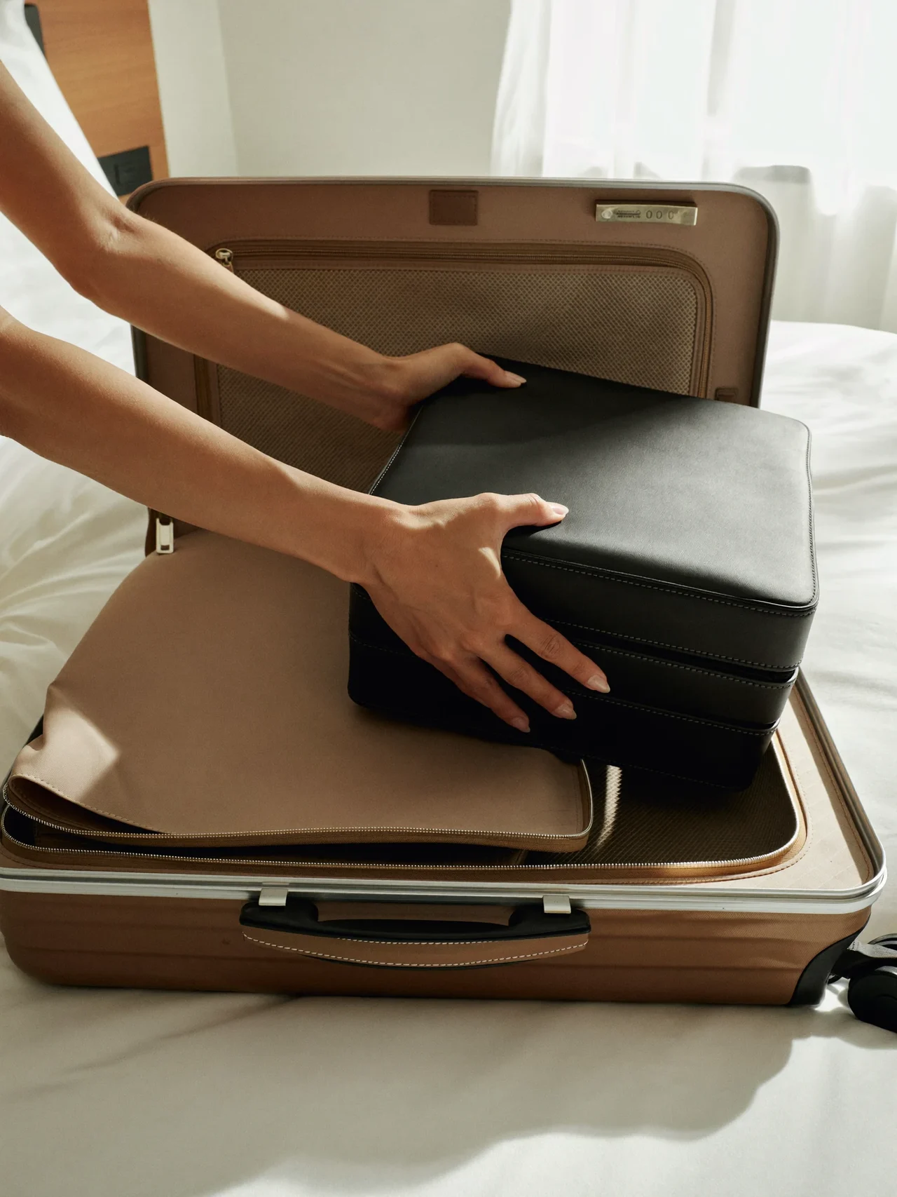 Hände beim Einpacken eines Würfels in einen Handgepäckkoffer im hellen Hotelzimmer.